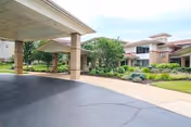 Covered porte-cochere and landscaped entrance of a two-story senior living building with columns and paved drive.