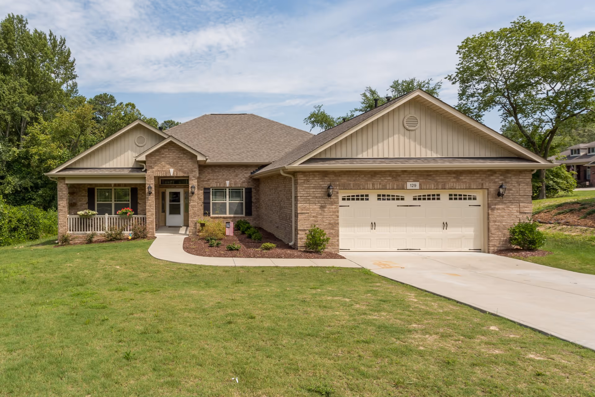 Single-story brick house with a front porch, two-car garage, and a grassy lawn.
