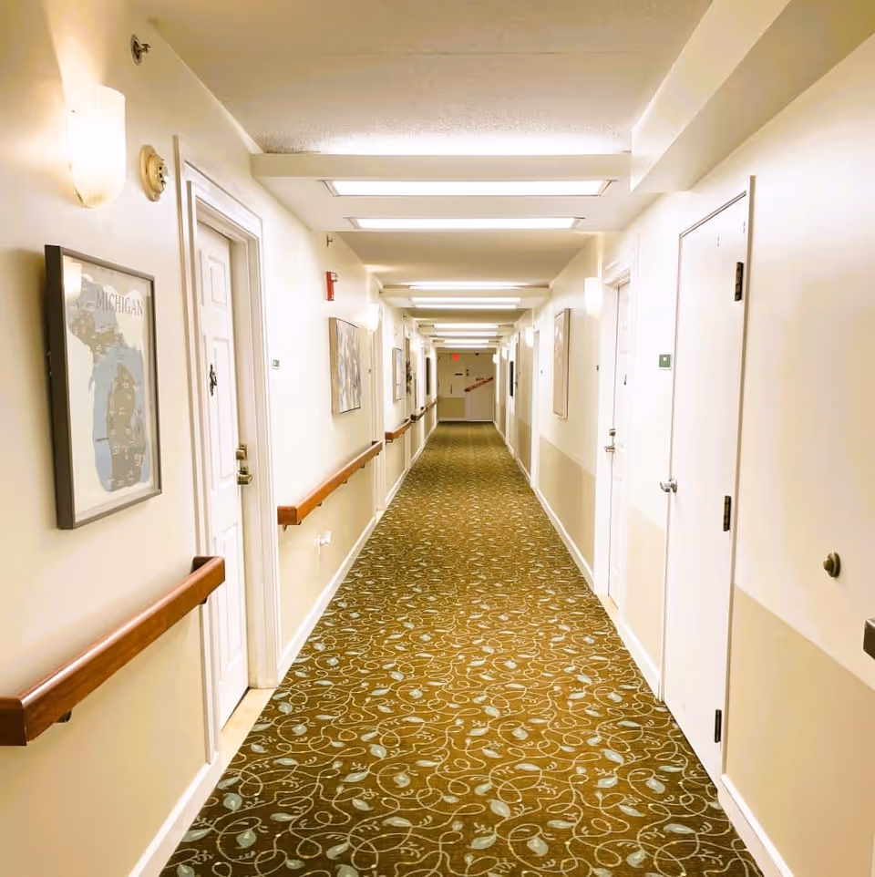 Long, well-lit interior hallway with patterned carpet, handrails, and doors on both sides.