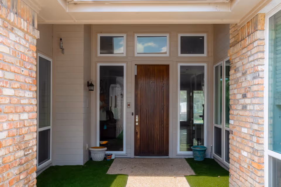 Exterior view of Lavendale Circle entrance with a wooden front door, sidelights, brick walls, and potted plants on the porch.