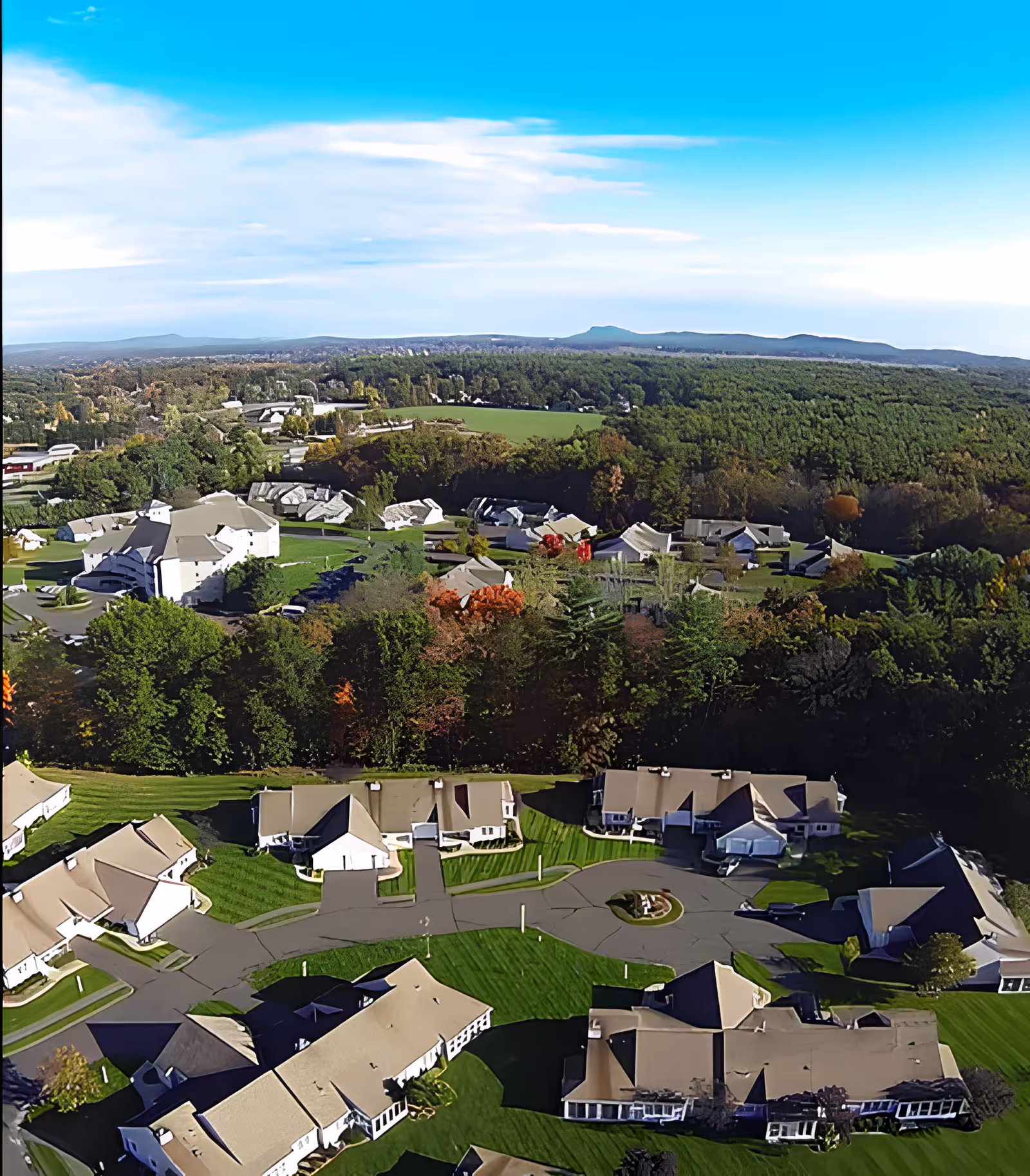 Aerial view of the American Inn campus showing multiple cottages and communal buildings surrounded by lawns, trees, and distant hills.