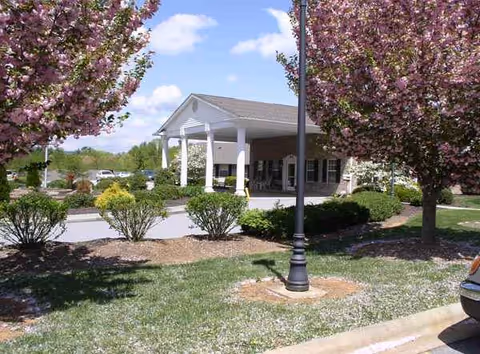 Senior living facility entrance with a covered porte-cochère, landscaped approach, and flowering trees.