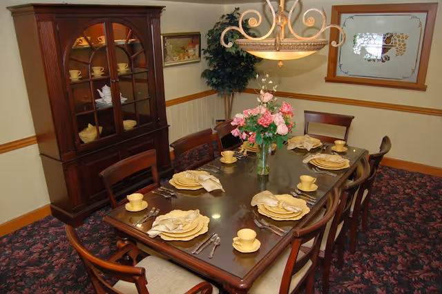Formal dining room with a wooden table set for eight, a floral centerpiece, chandelier, and a china cabinet.