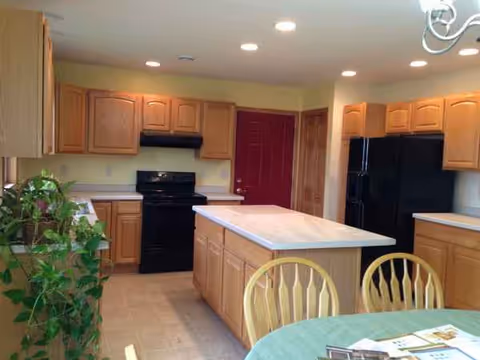 Bright kitchen with wooden cabinets, black appliances, and an island in a dining area.