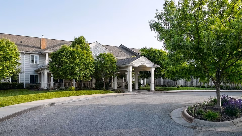 Front exterior view of Celebration Villa of Hearthstone (West) showing a two-story building with a covered entrance, surrounded by green trees and landscaping under a clear sky.