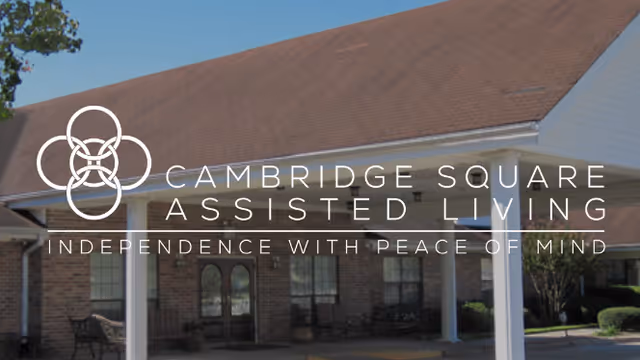 Front entrance of a brick assisted living building with a covered portico and an overlaid logo and facility name.