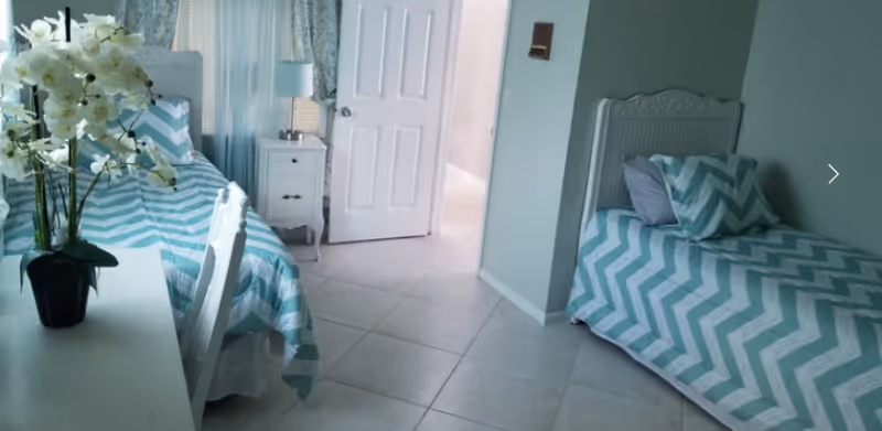 Two twin beds with teal chevron bedding flank a white nightstand in a bright bedroom.