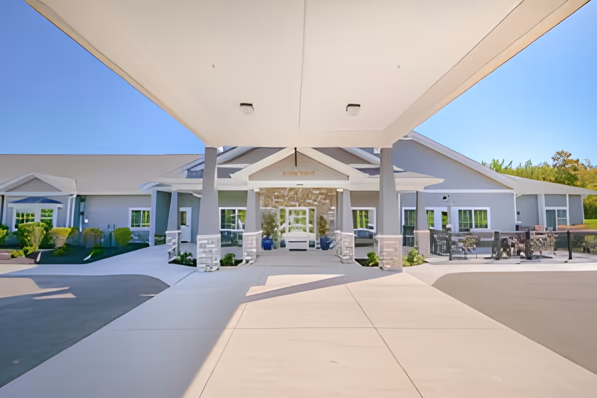 Covered porte-cochere and main entrance of a single-story senior living facility with outdoor seating and landscaping.