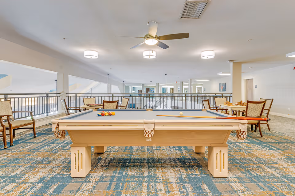 Interior common area featuring a pool table centered in a seating and game space with chairs and tables around it.
