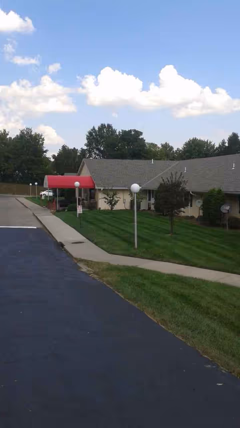 Exterior view of Maple Wood Healthcare Center with red canopy, walkway, and manicured lawn.