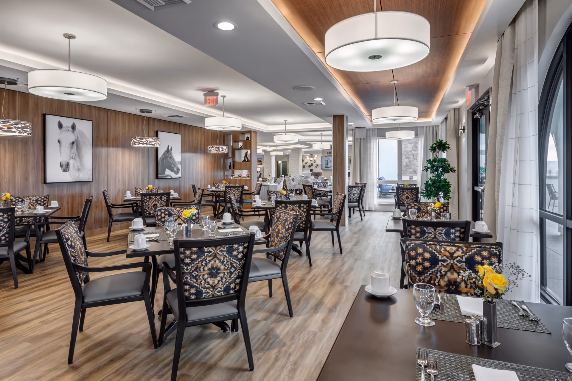 Spacious, modern dining room with multiple set tables, patterned chairs, wood-paneled walls, and large windows.