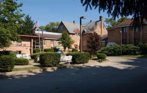 Exterior view of WBF Genoa City Retirement Home courtyard with benches and trees.