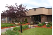 The Medilodge of Cheboygan exterior shows a beige building front with benches and landscaped shrubs.