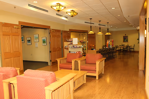 Bright communal room with wooden floors, upholstered armchairs and a dining area with pendant lights and a snack display.