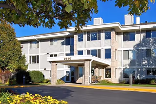 Front entrance of a three-story residential building with a covered entry displaying the number '2850', surrounded by landscaping and trees.