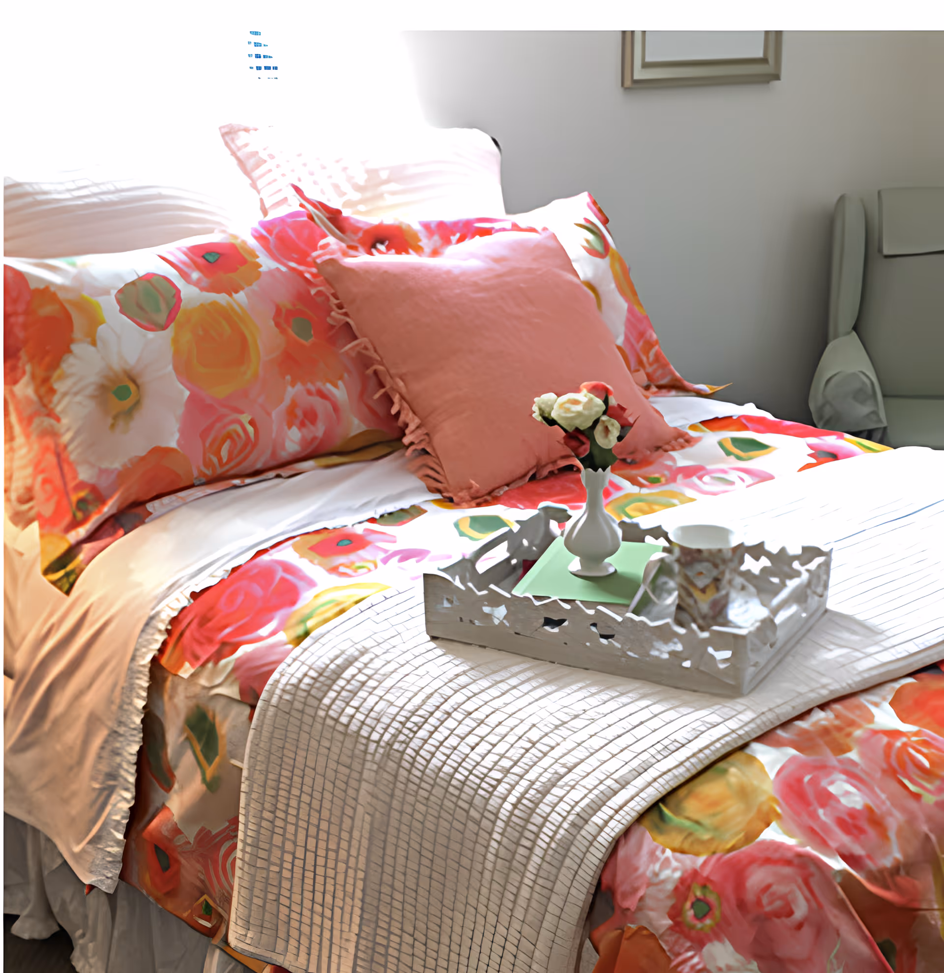 Bed with colorful floral bedding, a pink throw pillow, and a decorative tray holding a small vase and cup.
