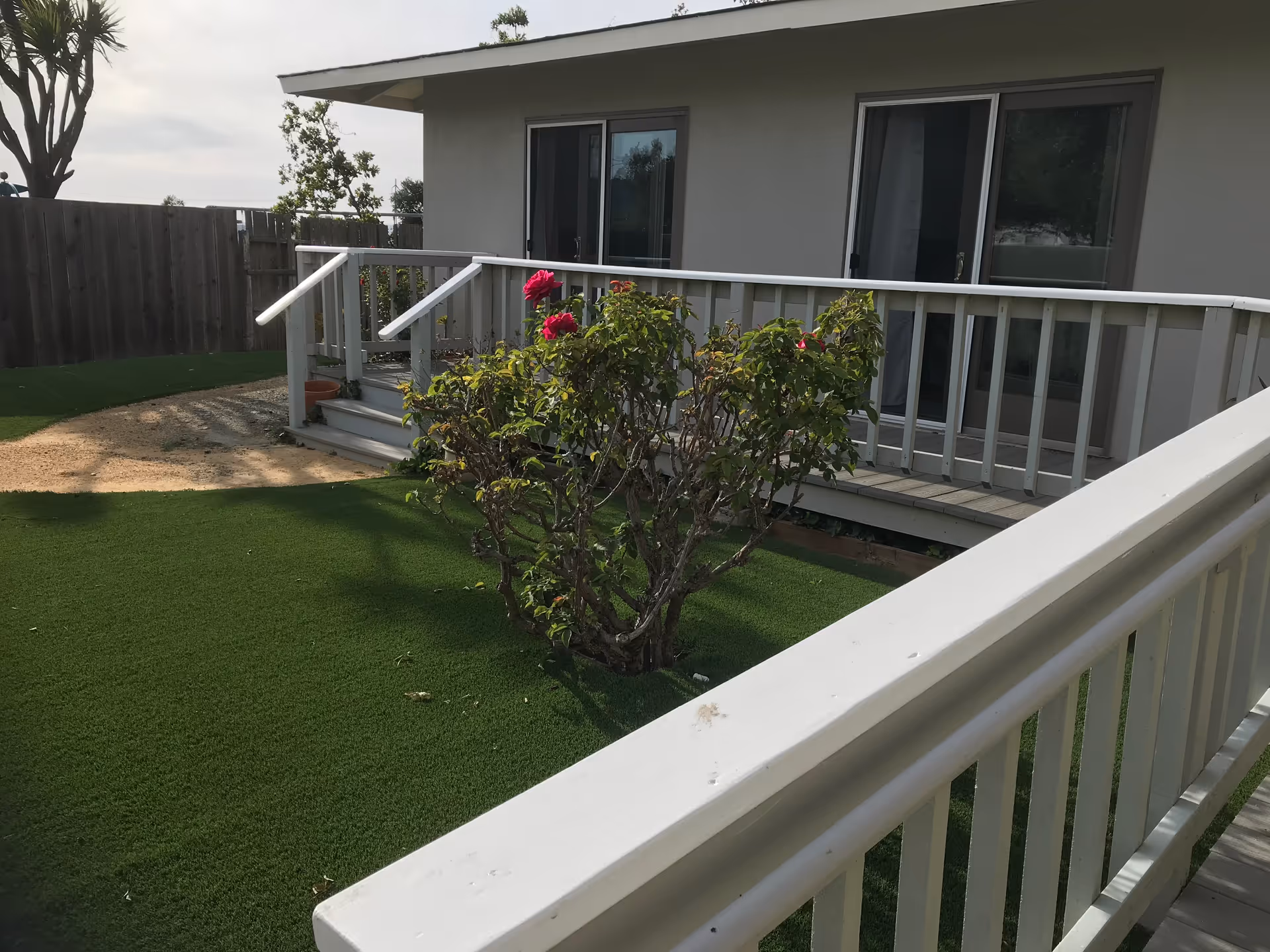 White-railed porch and ramp leading to sliding glass doors, with artificial turf and a flowering shrub in the yard.