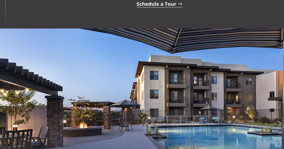 Outdoor pool and patio area with umbrellas, a fire pit and pergola in front of a multi-story apartment building.