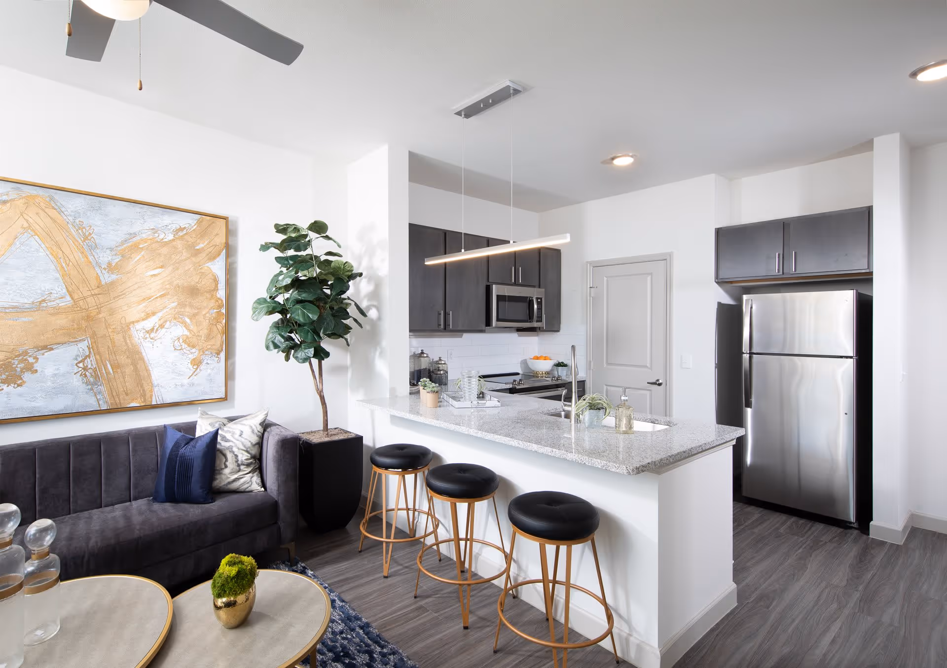 Open-plan living area with a modern kitchen island, three bar stools, stainless steel appliances and a sofa.