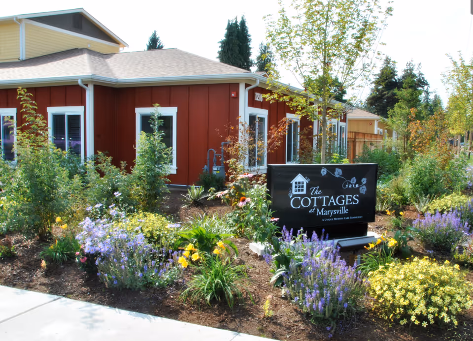 Red cottage-style building with blooming garden and The Cottages at Marysville sign