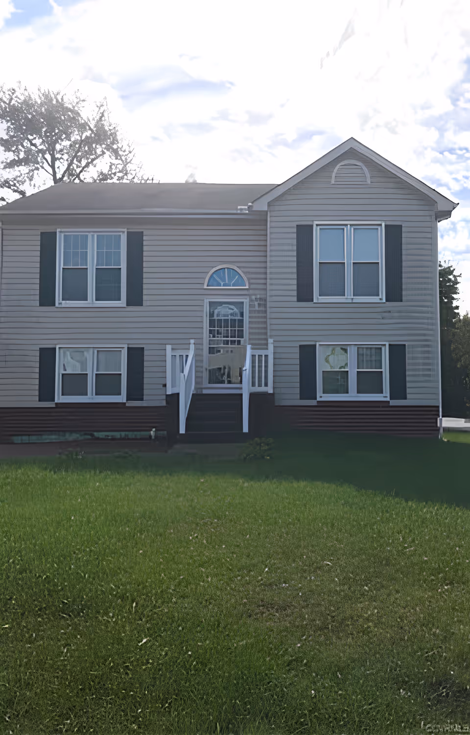 Front exterior of a two-story light-gray siding house with a central glass door, white steps, and a grassy lawn.