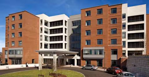 Exterior view of the Leonard Florence Center for Living, a multi-story brick-and-white building with a covered entrance, driveway and parked cars.