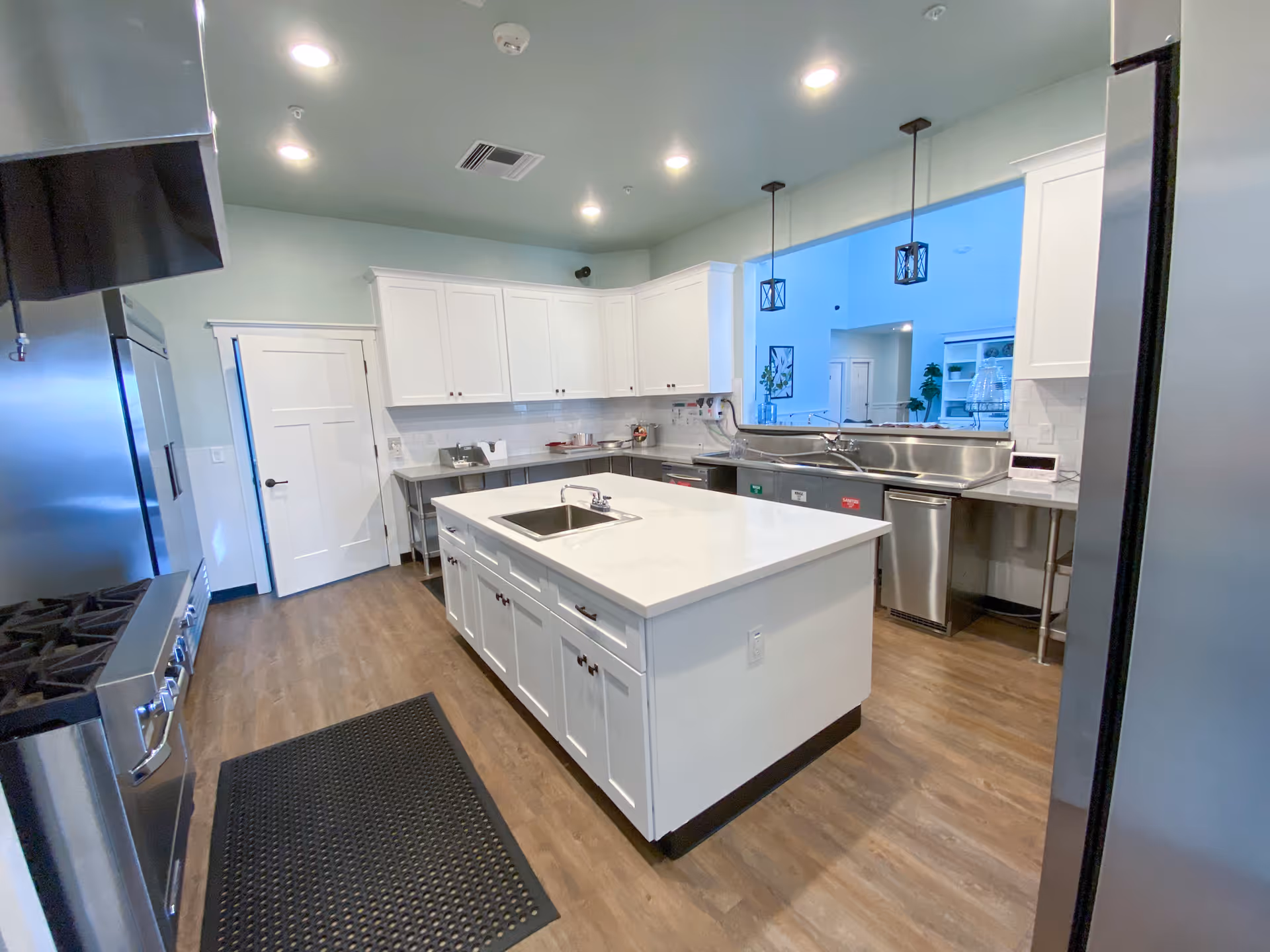 Bright modern kitchen with a central island, white cabinets, stainless-steel appliances, and pendant lights.