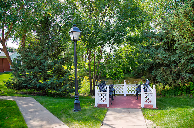 Outdoor patio with chairs on a red deck surrounded by trees.