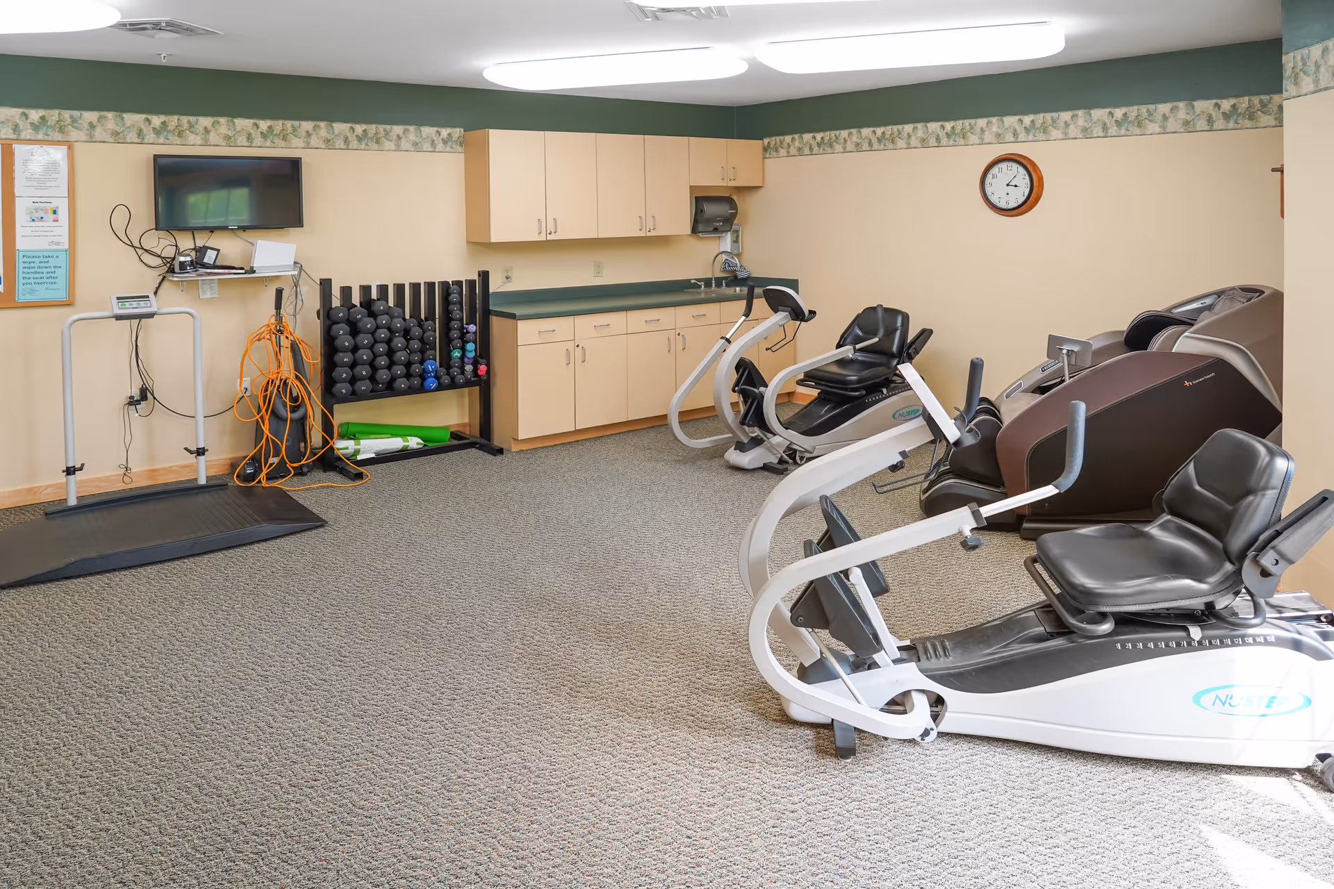 Exercise room with several recumbent bikes, free weights, a TV, and storage cabinets.