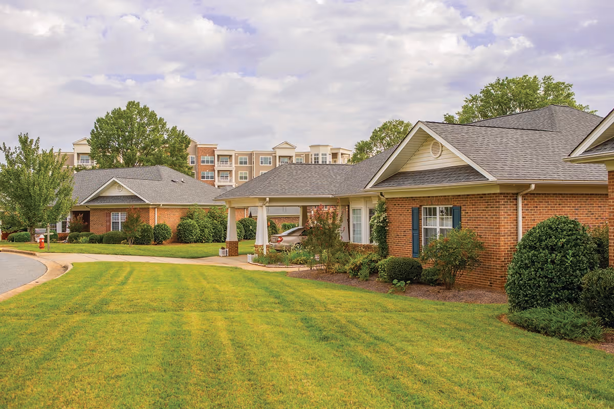 Front exterior of single-story brick senior living cottages with a manicured lawn and a multi-story building in the background.