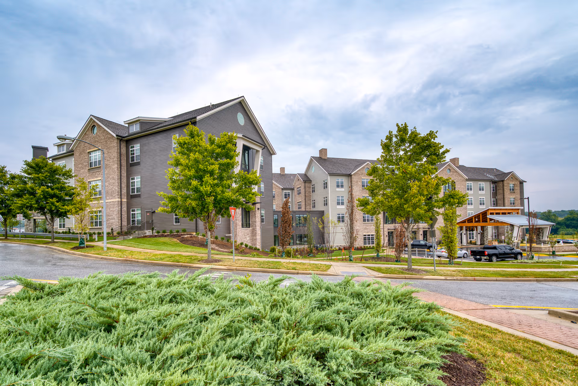 Exterior view of Tribute at Melford senior living campus with trees and parked cars.