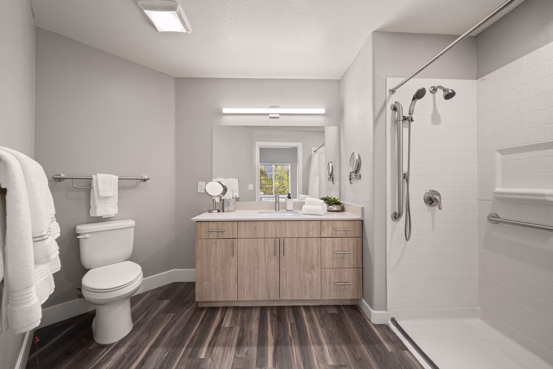 Modern bathroom with a wooden vanity and mirror, toilet, towel racks, and a walk-in shower.