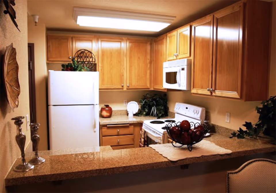 Compact kitchen with wooden cabinets, a white refrigerator and stove, and a granite countertop with decorative items.