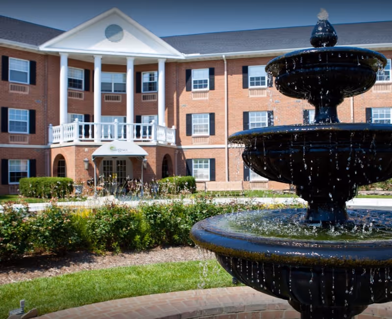 A tiered water fountain in front of a three-story brick building with white columns and balconies.