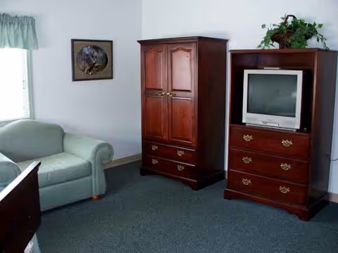 A living room in a senior facility with a sofa, armoire, and TV.