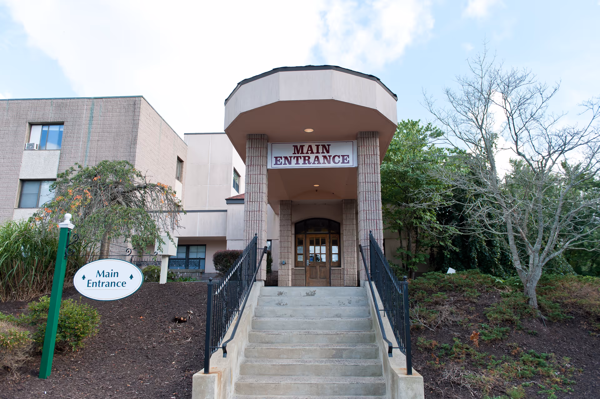 Front steps leading up to the main entrance of a senior living facility with a covered portico and a 'Main Entrance' sign.