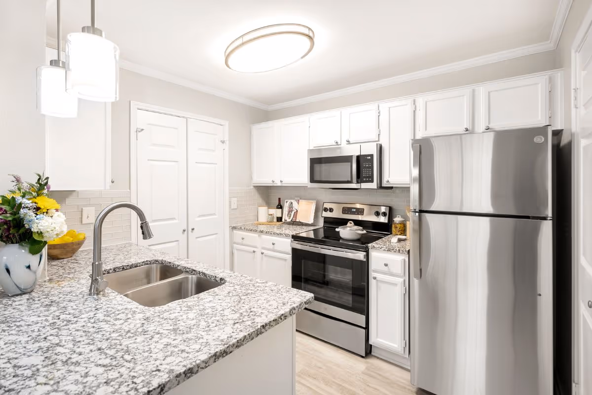 Bright modern kitchen with granite countertops, stainless steel refrigerator and stove, white cabinets, and an island sink.