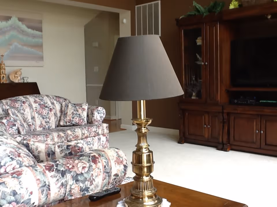Cozy living room with floral upholstered sofas, a brass table lamp on a coffee table, and a wooden entertainment center.