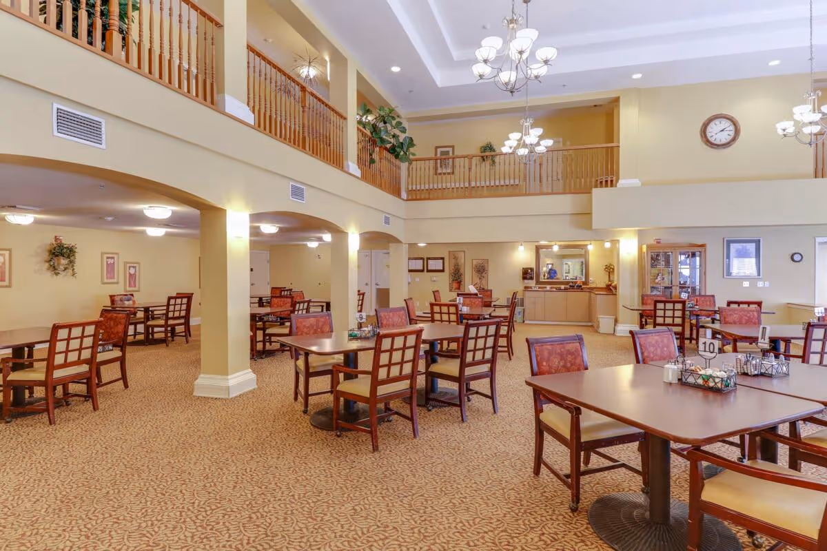 Spacious two-story dining room with multiple tables and chairs, chandeliers, and a balcony railing overlooking the area.