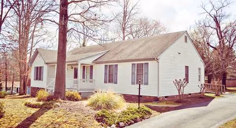 A single-story white building with a small front porch, trees, and a driveway.