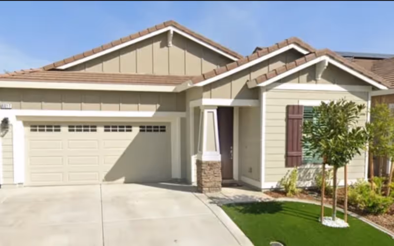 Single-story suburban house front with an attached two-car garage, small covered porch, and a landscaped yard.