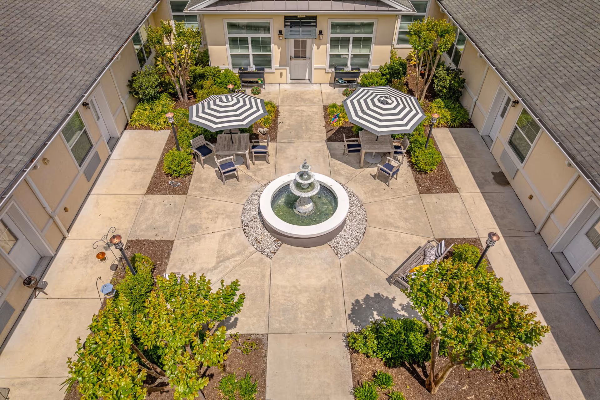 Aerial view of a central courtyard with a fountain, striped umbrellas, seating areas, and surrounding building entrances.