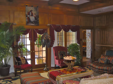 Wood-paneled living room with plush seating, plants, and a central fruit bowl centerpiece.