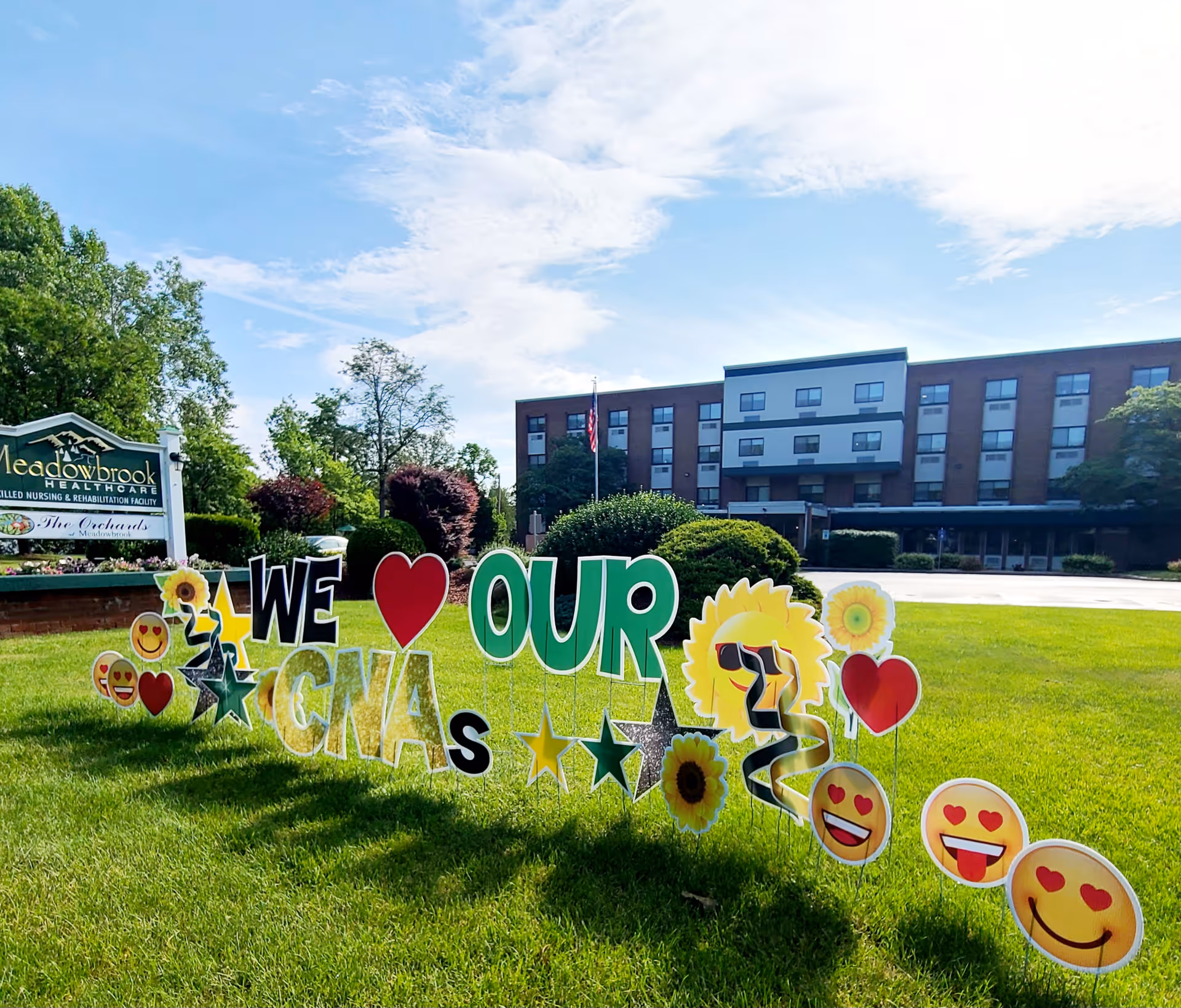 Front lawn of Meadowbrook Healthcare with colorful yard signs reading 'We ♥ Our CNAs' and the facility building in the background.