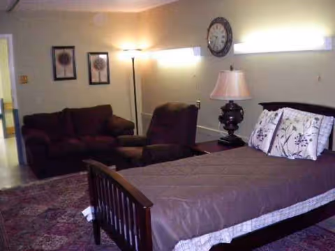 A furnished bedroom with a bed, seating area, lamp, clock, and wall art.