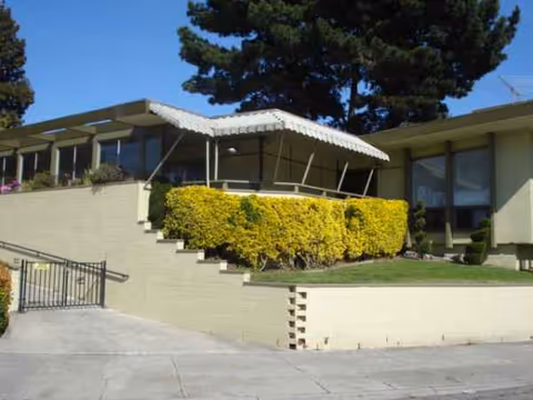 Exterior view of Marina Garden Nursing Center showing stairs, a covered entry, and trimmed shrubs.