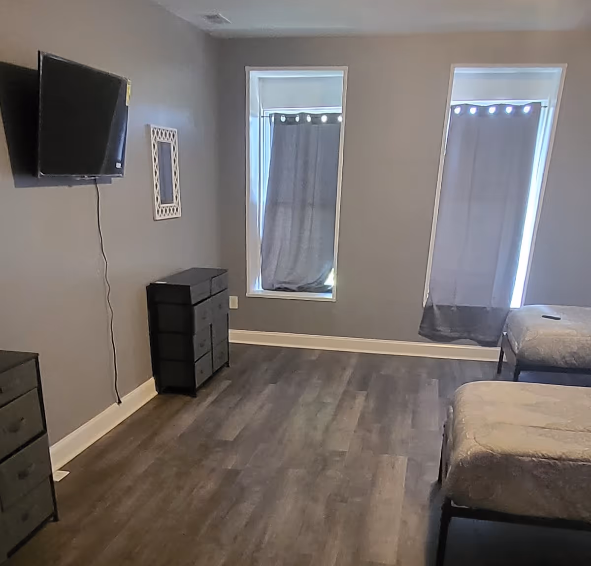 Two twin beds with gray bedding, dressers, and a wall-mounted TV.