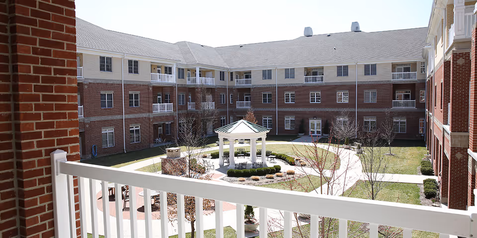 View from a balcony over a landscaped central courtyard with a gazebo surrounded by a three-story brick senior living building.
