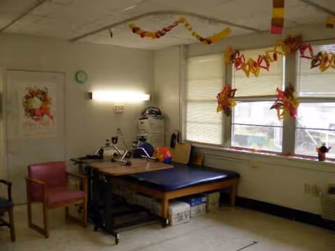 Therapy room with a padded treatment table, chairs, and colorful garland decorations.