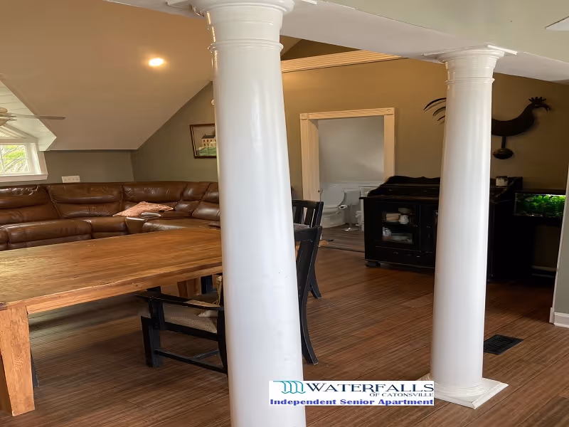 Open living/dining area with two white columns, wooden table, leather sectional sofa and a cabinet with a fish tank.